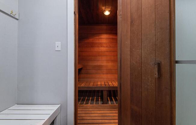 A wooden sauna with benches inside and a doorway leading to it.