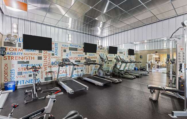 A gym with a variety of equipment and a wall covered in fitness related words.