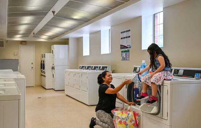 two young girls sitting on washing machines in a laundry room at Hamilton Manor Apartments, Hyattsville, MD 20782