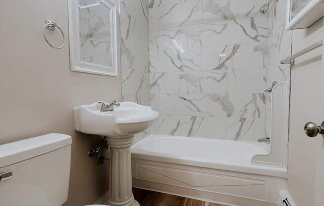 A white toilet sits next to a white sink in a bathroom with a marble wall.