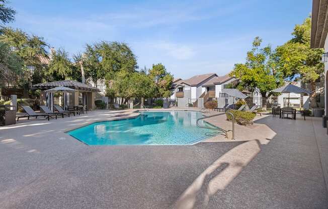 A swimming pool surrounded by a concrete patio and lounge chairs.