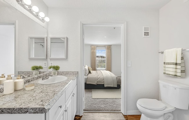 a bathroom with a toilet sink and mirror and a bedroom in the background