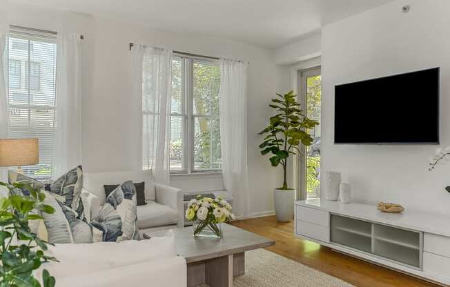 A living room with a white couch, a wooden coffee table, and a large flat-screen TV mounted on the wall.