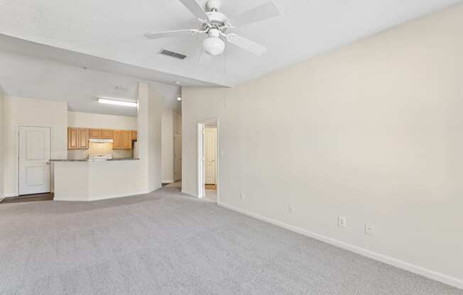 an empty living room with a ceiling fan and a kitchen