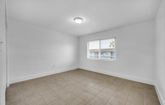 an empty living room with a window and a tiled floor