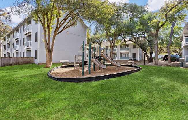A playground with a slide and a green lawn in front of apartment buildings.