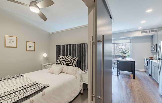 A bedroom with a bed, a ceiling fan, and a door leading to a kitchen.