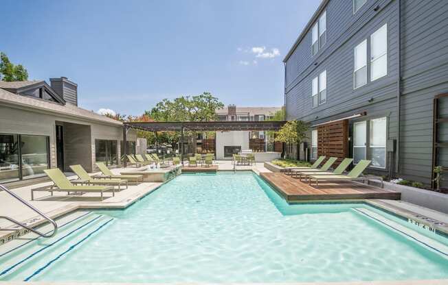 a swimming pool with lounge chairs and a wooden diving board in front of a gray building
