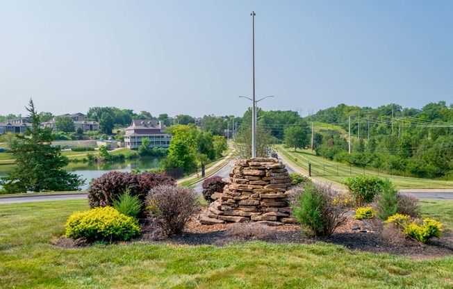 a stone wall surrounded by landscaping in front of a road and a river