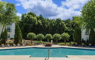 a swimming pool with chaise lounge chairs and trees in the background at Whitehall Estate apartments in Charlotte NC