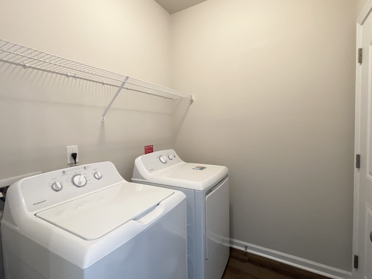 two washers and a dryer in a laundry room with a shelf above them
