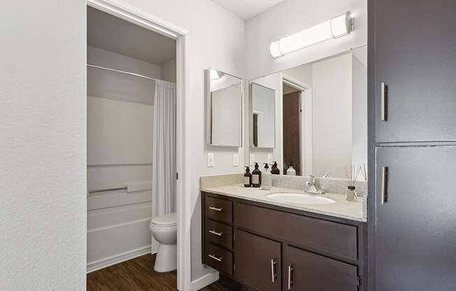 Model Bathroom with Dark Wood Cabinets, Wood-Style Flooring and Shower/Tub at Creek at 2645 Apartments located in Sacramento, CA.