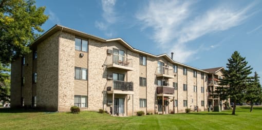 a brick apartment building with balconies and a green lawn