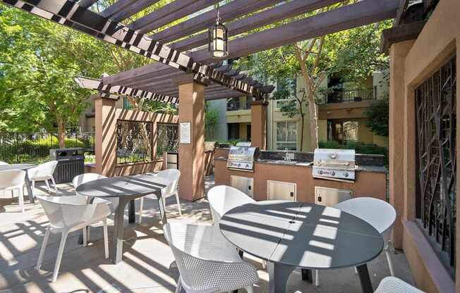 A patio with white chairs and tables is covered by a striped awning at The Kitt at Warner Center Apartments, Woodland Hills, CA, 91303