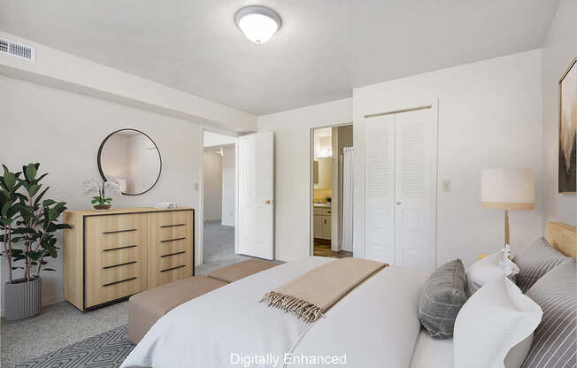 A bedroom with an ensuite, a bed, nightstand, and a plant at The Highlands Apartments in Elkhart, IN