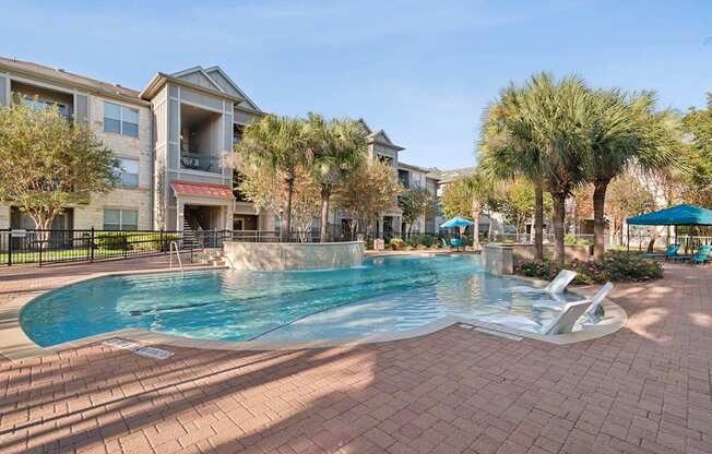 A swimming pool surrounded by a brick patio and palm trees.