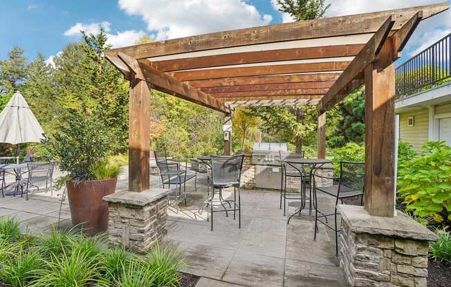 A wooden pergola over a patio with chairs and tables with a bbq.