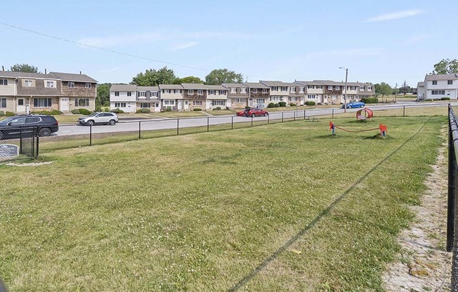 a grassy area with a fence and houses in the background