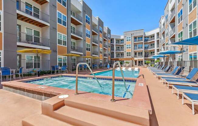a pool with lounge chairs and umbrellas in front of an apartment building