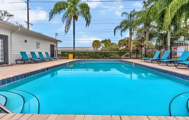 A swimming pool surrounded by lounge chairs and palm trees.