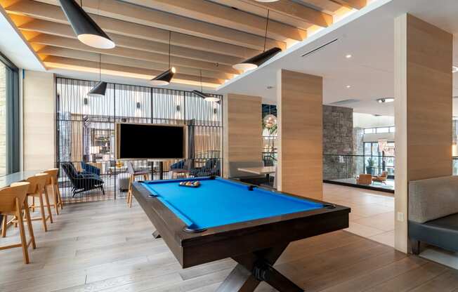 a pool table sits in the middle of a room with a tv on the wall  at Century West Pryor, Lee's Summit, Missouri