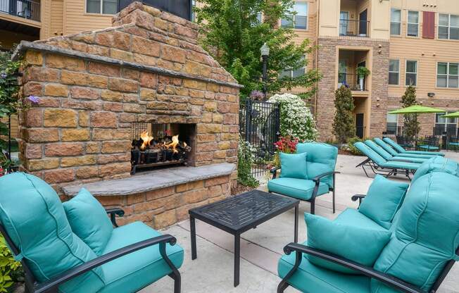 Outdoor stone fire place surrounded by cozy chairs  and a coffee table.