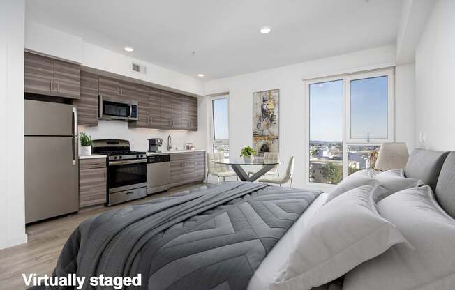 A modern bedroom with a large bed and a kitchen area in the background.