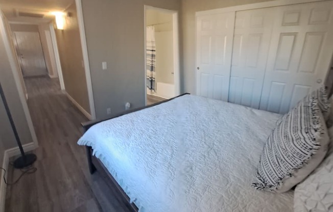 A bedroom with a bed, pillows, and a wooden floor.