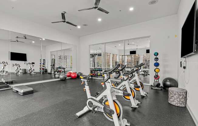 A gym with a row of stationary bikes and a television on the wall.