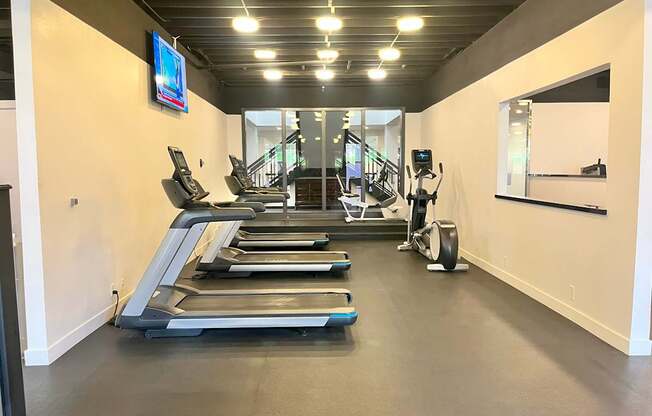 A gym with treadmills, elliptical machines, and a mirror.