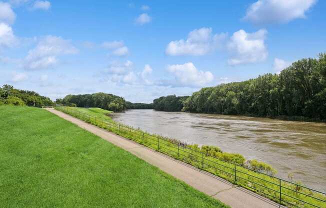 A river flows through a green landscape with a fence alongside a walkway.