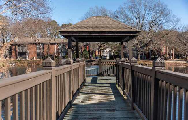 A wooden gazebo sits on a wooden bridge over a body of water.