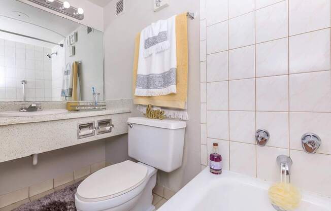 A white toilet sits in a bathroom with a white sink and a white towel hanging on the wall.