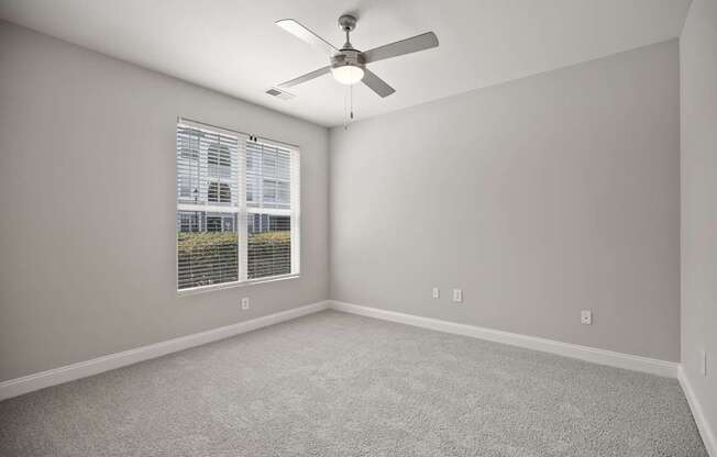 A room with a ceiling fan and a window with blinds.