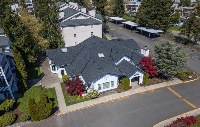 A white building with a grey roof is surrounded by trees and bushes.