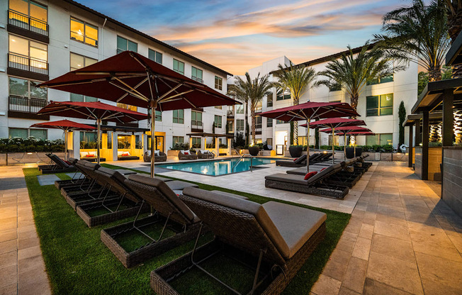 Poolside retreat with red umbrellas, plush loungers, and a glowing sunset backdrop