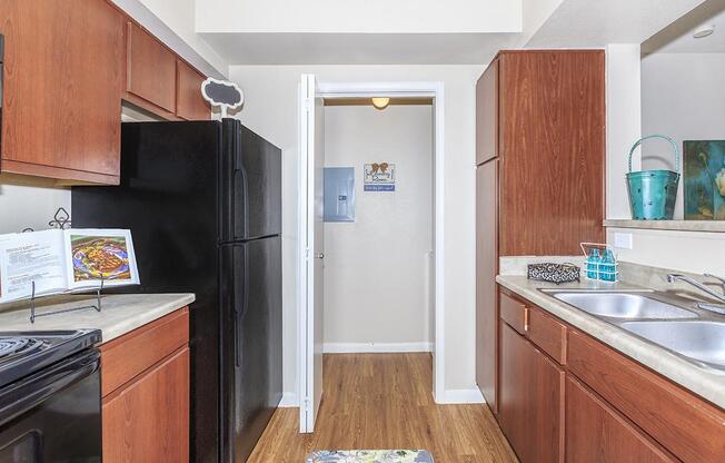 Galley-style kitchen with brown cabinetry, black appliances, and access to full-size washer/dryer