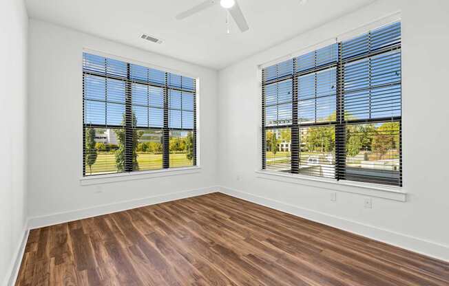 A room with wooden floors and two windows with blinds.