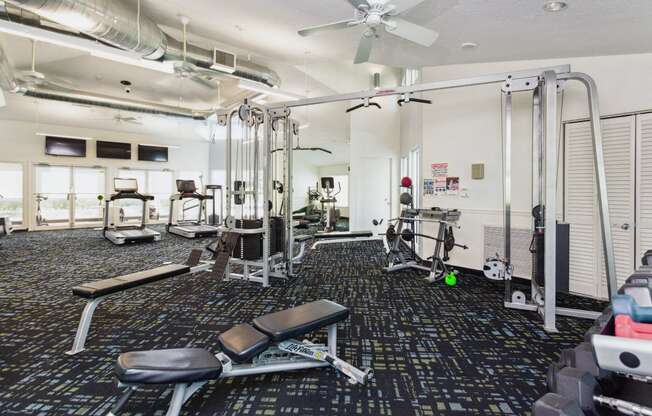 a gym with cardio equipment on the floor and a ceiling fan