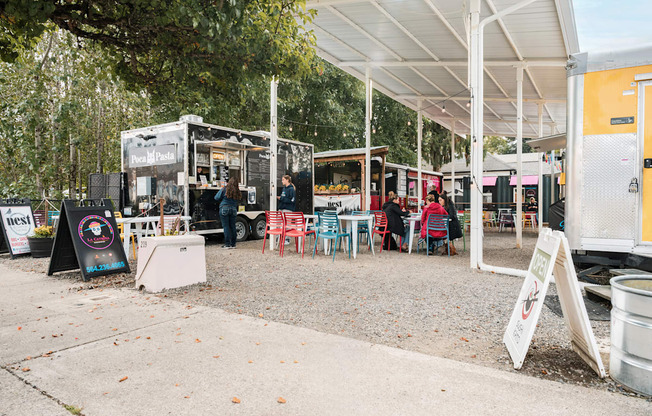 A food truck is parked under a white canopy with several people seated at tables outside.