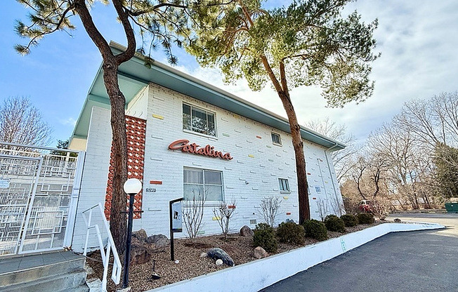 Charming white apartment building with unique exterior, surrounded by lush greenery and a spacious driveway.