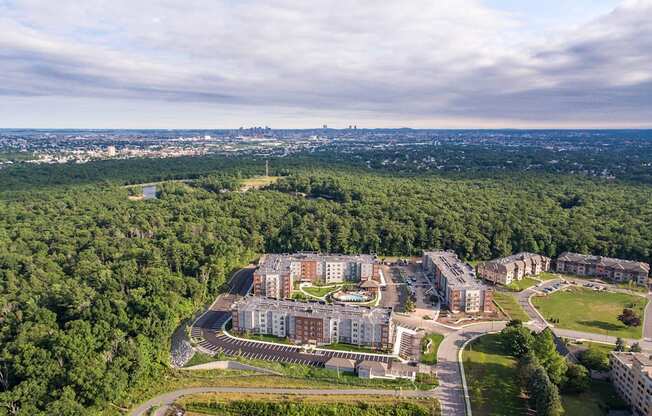 an aerial view of an apartment complex with trees and a city in the background