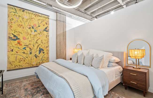 A bedroom with a large floral print on the wall and a bed with a blue comforter.