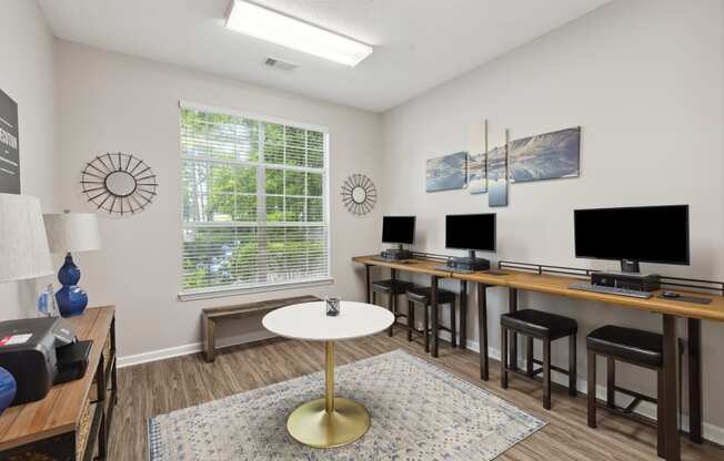 a living room with desks and chairs and a table with computer monitors