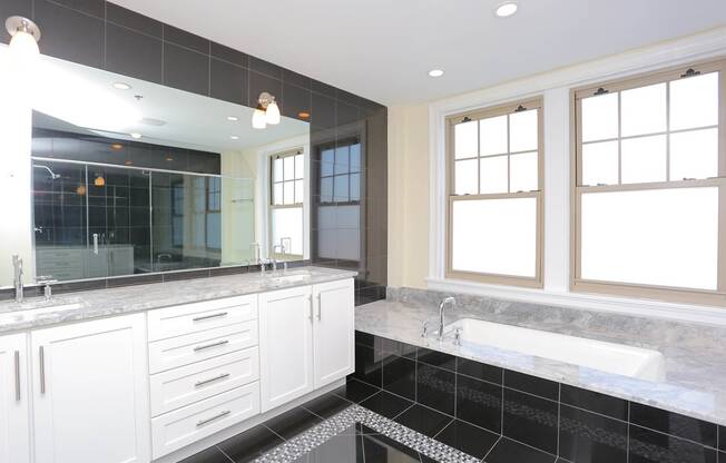 Penthouse bathroom with set in bathtub surrounded by dark tile, white vanity and mirror at York House, Saint Louis, Missouri