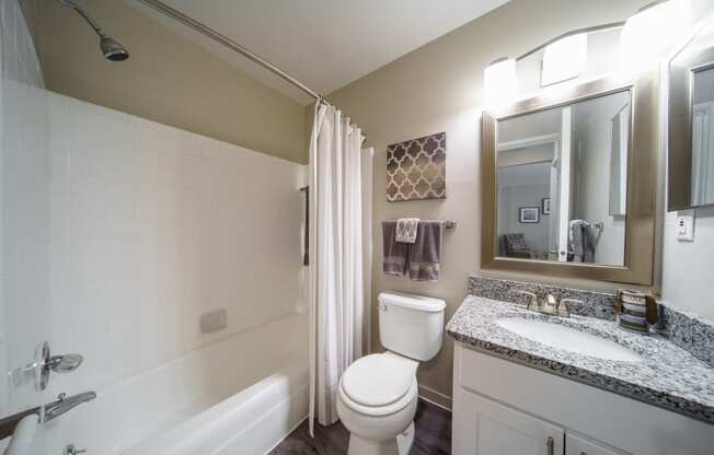 Bathroom with tub/shower combo, white cabinets, modern grey and white counters.