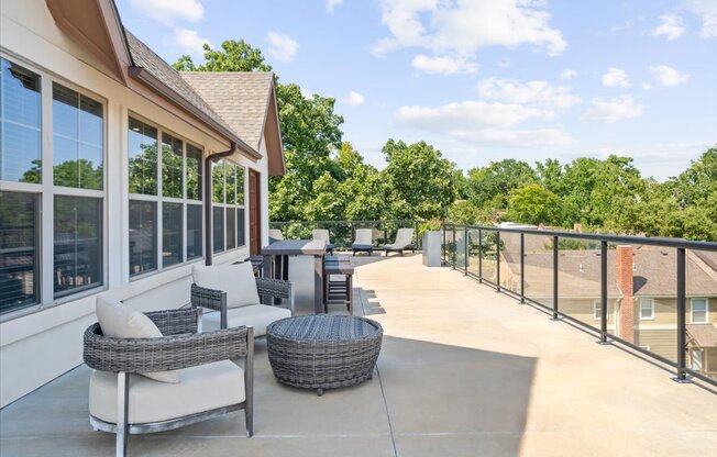 A patio with a table and chairs overlooking a tree-filled neighborhood.