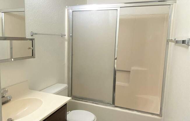 A white toilet sits in a bathroom next to a sink and a walk-in shower.