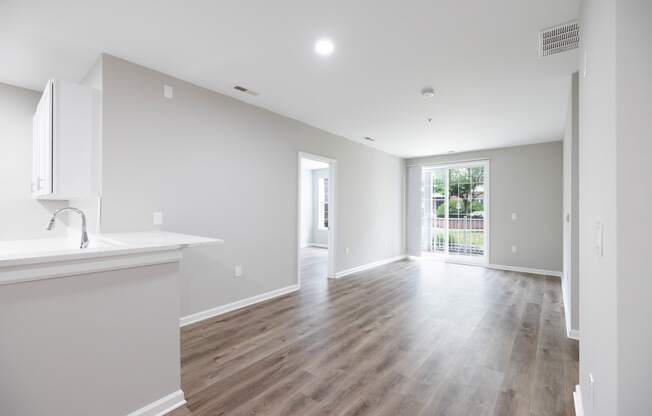 a renovated living room and kitchen with white walls and wood flooring