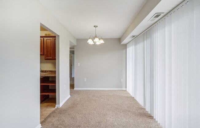 a hallway with white curtains and a carpeted floor and a door to a kitchen